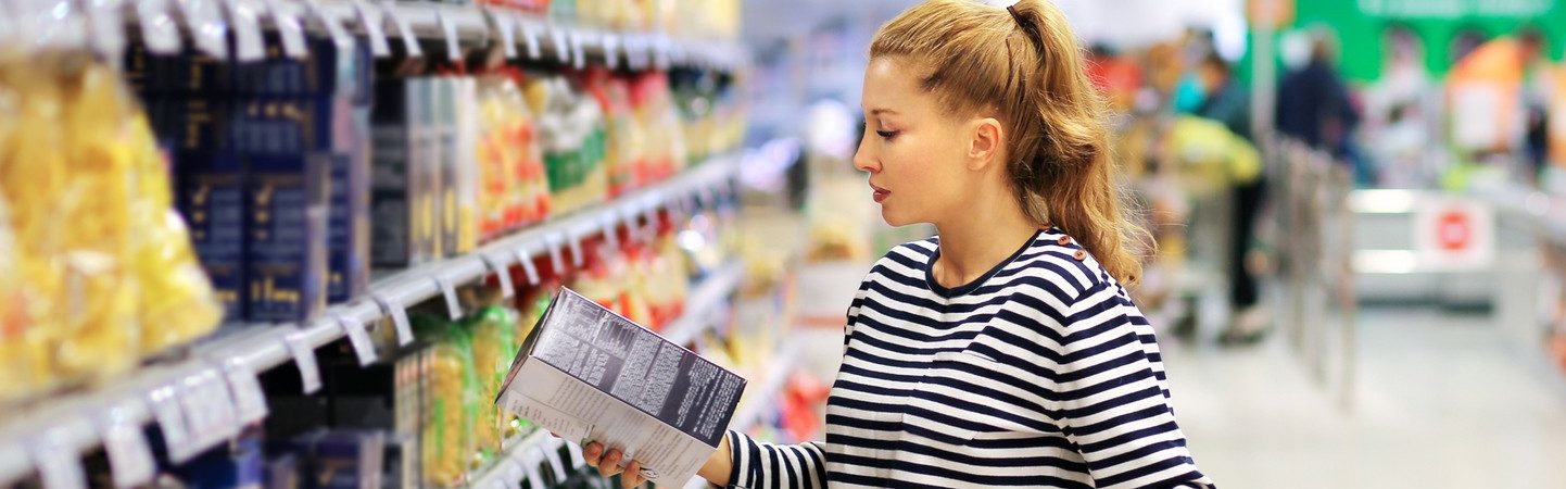 Woman shopping in supermarket reading product information.